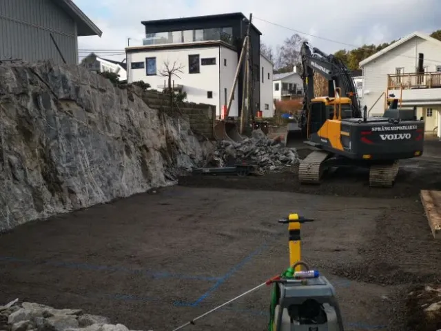 Grävmaskin och packad markbädd intill en bergvägg