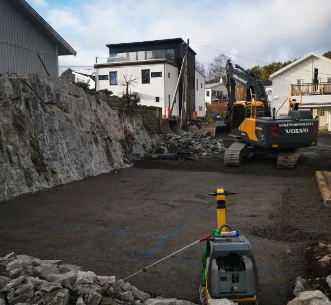 Grävmaskin och packad markbädd intill en bergvägg och nya villor